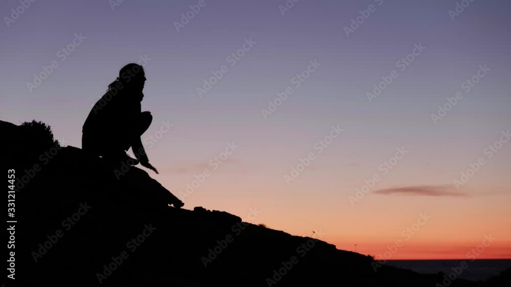 Woman sitting on a rock at sunset, Ibiza Woman sitting on a rock at sunset, Ibiza