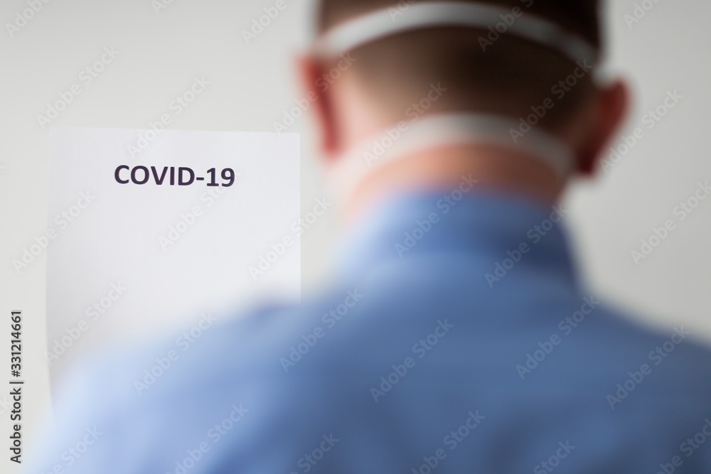 mężczyzna w masce ochronnej spoglądający w napis COVID-19 - obrazy, fototapety, plakaty 