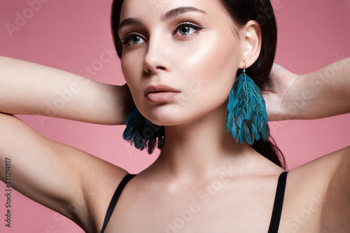 Beautiful young woman with bird feathers earrings over pink photo