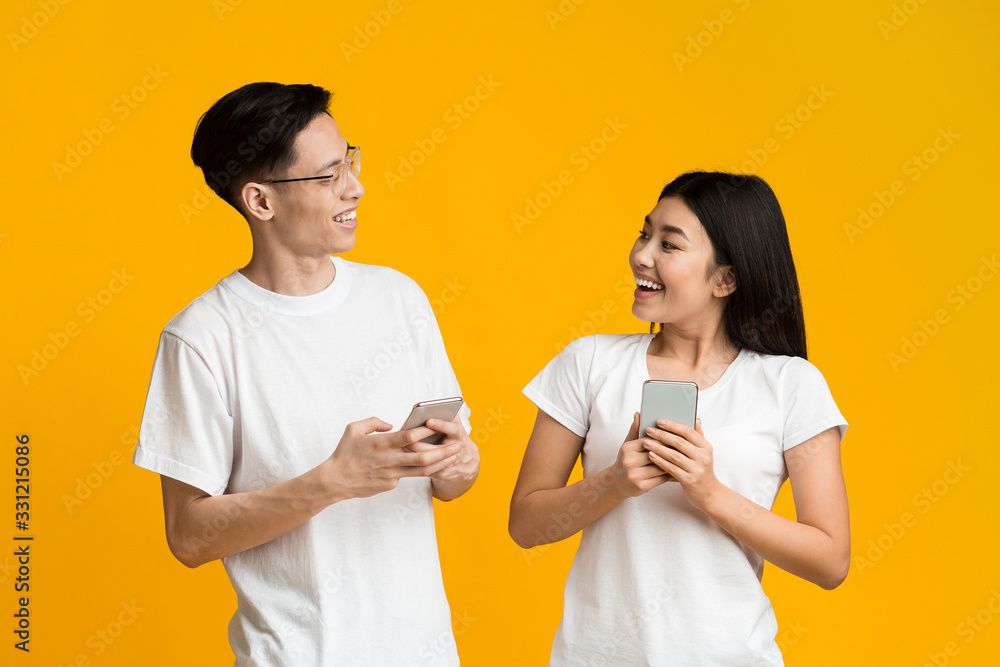 Happy asian couple looking at each other while using smartphones Happy asian couple looking at each other while using smartphones