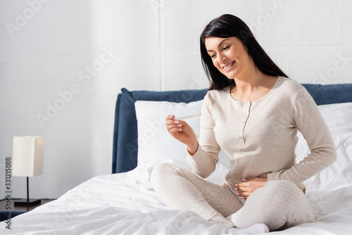 happy woman holding pregnancy test and sitting on bed © LIGHTFIELD STUDIOS