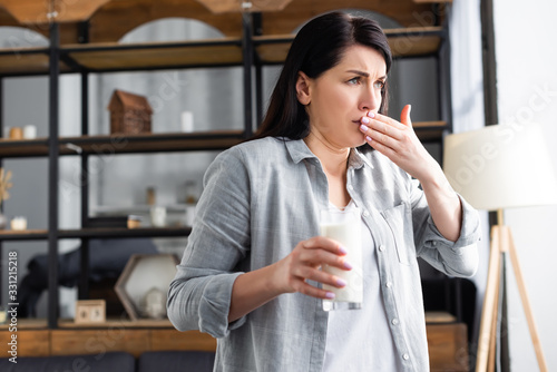 Fotografie woman with lactose intolerance holding glass of milk and covering mouth