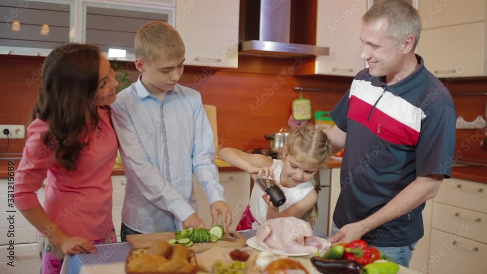 Happy family parents, daughter and son cutting fresh vegetable salad having fun cooking together in kitchen, parents teaching funny children help prepare food meal at home. Cooking roasted chicken Happy family parents, daughter and son cutting fresh vegetable salad having fun cooking together in kitchen, parents teaching funny children help prepare food meal at home. Cooking roasted chicken