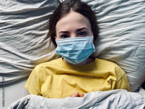 a teenage girl in a medical mask in bed during corona virus quarantine time lack of freedom