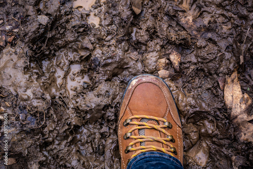The leather boots on the hiking foot are immersed in the muddy road.