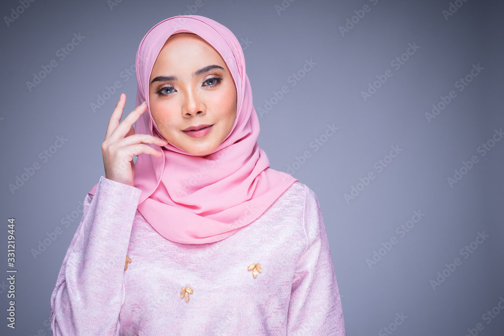 Headshot portrait of a beautiful female model wearing traditional dress and hijab, a lifestyle apparel for Muslim women isolated on grey background. Idul Fitri and hijab fashion concept. Headshot portrait of a beautiful female model wearing traditional dress and hijab, a lifestyle apparel for Muslim women isolated on grey background. Idul Fitri and hijab fashion concept.