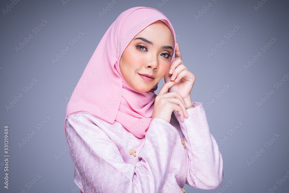 Headshot portrait of a beautiful female model wearing traditional dress and hijab, a lifestyle apparel for Muslim women isolated on grey background. Idul Fitri and hijab fashion concept. Headshot portrait of a beautiful female model wearing traditional dress and hijab, a lifestyle apparel for Muslim women isolated on grey background. Idul Fitri and hijab fashion concept.