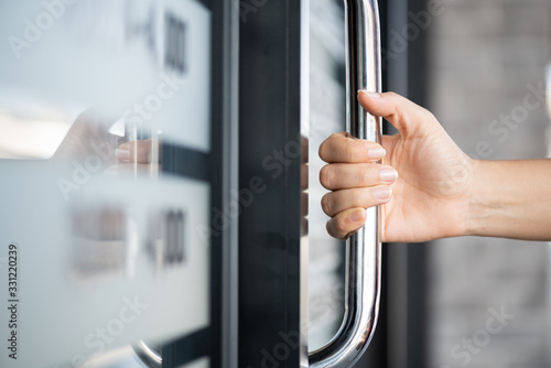 Closeup woman hand holding the door bar to open the door with glass reflection background. photo