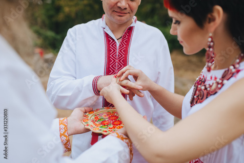 The wedding ceremony of the newlyweds in embroidered clothes, in the old Ukrainian traditions of paganism. Ethnic rite for newlyweds in Ukraine. The bride and groom put on gold rings to each other. photo