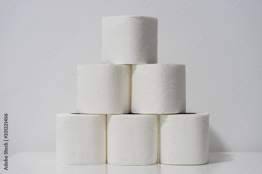 Front view on white toilet paper rolls stacked on the table in front of the wall background Front view on white toilet paper rolls stacked on the table in front of the wall background