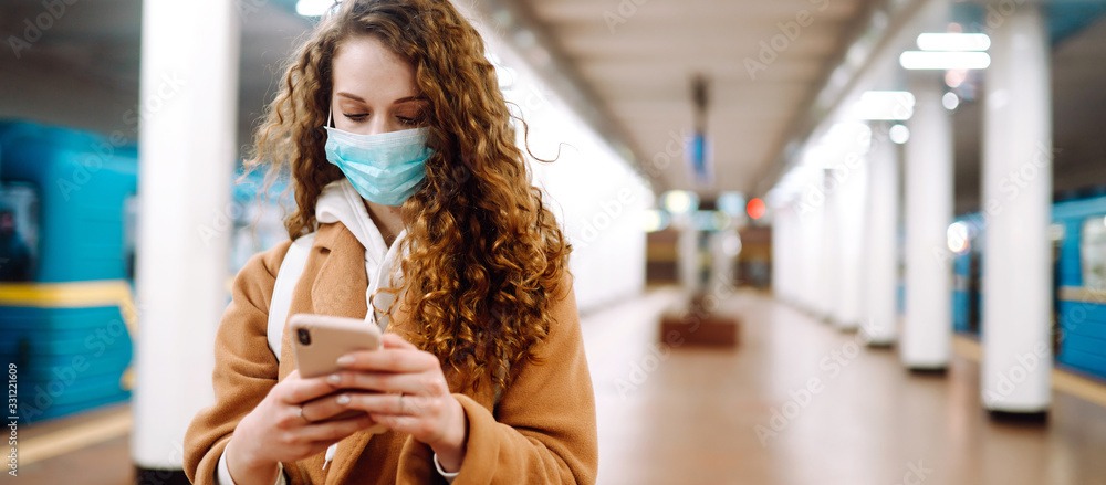 Long edge. Girl in protective sterile medical mask watching news on the phone about coronavirus in subway tunnel. The concept of preventing the spread of the epidemic. - obrazy, fototapety, plakaty 