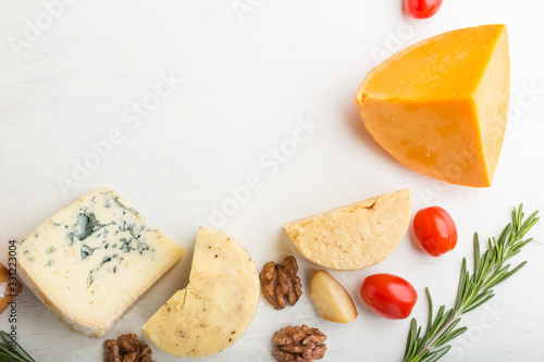 Set of different types of cheese with rosemary and tomatoes on a white wooden background . Top view, copy space.