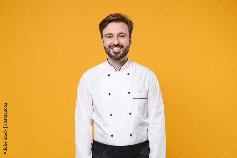 Smiling young bearded male chef cook or baker man in white uniform shirt posing isolated on yellow orange wall background studio portrait. Cooking food concept. Mock up copy space. Looking camera. Smiling young bearded male chef cook or baker man in white uniform shirt posing isolated on yellow orange wall background studio portrait. Cooking food concept. Mock up copy space. Looking camera.