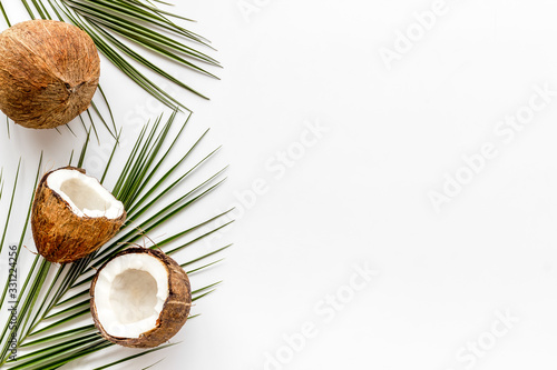 Coconuts frame. Nuts pieces and exotic leaves on white background top-down copy space