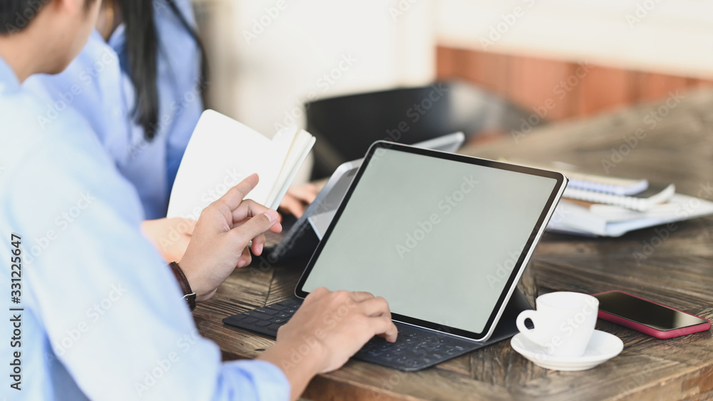 Cropped image of graphic designer team working together with computer tablet and document/information at the wooden meeting table over vintage office as background. Cropped image of graphic designer team working together with computer tablet and document/information at the wooden meeting table over vintage office as background.