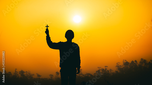 human lift christian cross up to sky with praying and worship God at sunset background. christian silhouette concept.