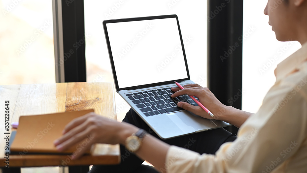 Cropped image of smart man working with white blank screen computer laptop while sitting at the wooden working desk over modern office as background. Cropped image of smart man working with white blank screen computer laptop while sitting at the wooden working desk over modern office as background.