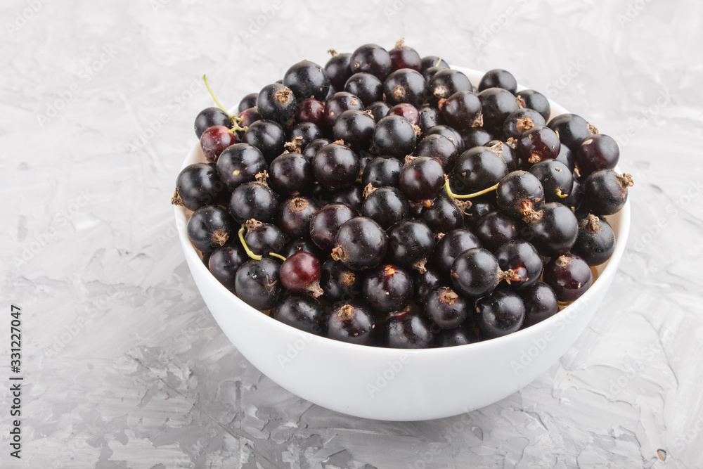 Fresh black currant in white bowl on gray concrete background. side view. Fresh black currant in white bowl on gray concrete background. side view.