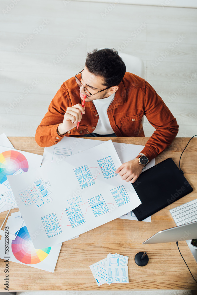 Overhead view of pensive designer working with templates of user experience design on table Overhead view of pensive designer working with templates of user experience design on table
