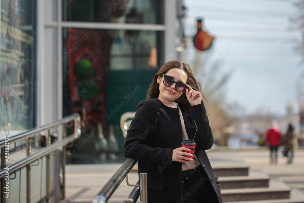 cheerful woman on a city street drinks coffee on a sunny day and looks at the camera. coffee to go. Portrait of a girl with a drink in hands cheerful woman on a city street drinks coffee on a sunny day and looks at the camera. coffee to go. Portrait of a girl with a drink in hands