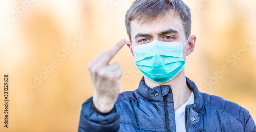 Fotografi Young man with protective mask shows obscene gesture - fucker