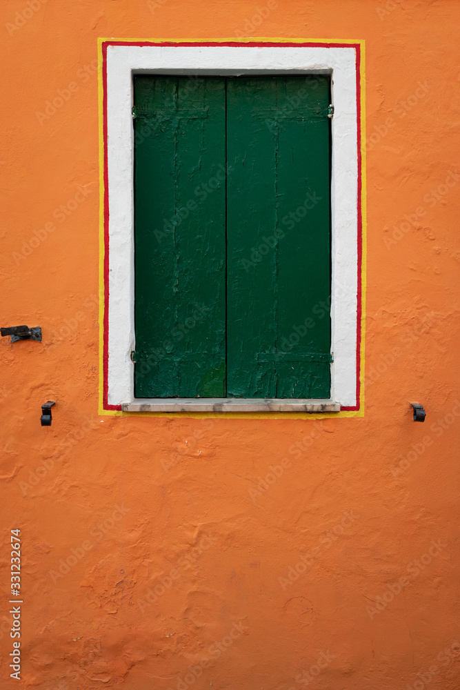 Window with closed green shutters on an orange wall