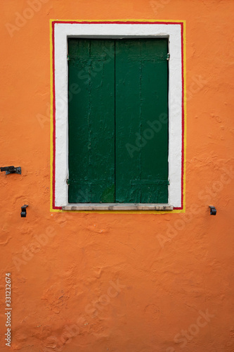 Window with closed green shutters on an orange wall
