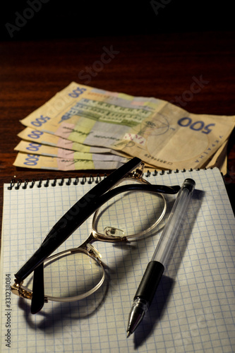Notebook glasses pens and money on the table.