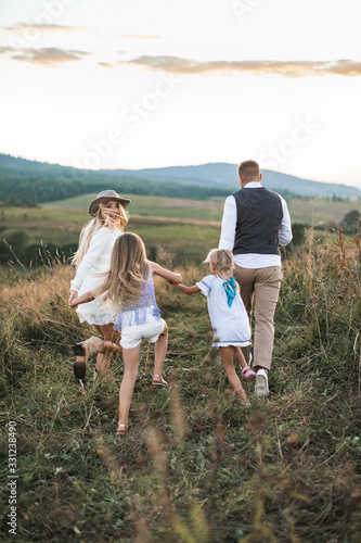 Summertime in the countryside. Back view of the family with two little daughters running and having fun in the summer wild field at the sunset.