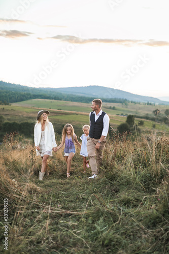 Happy family  father  mom  and two cute girls in casual boho wear walking together in field at sunset. The concept of harmony  family and love  happiness and joy