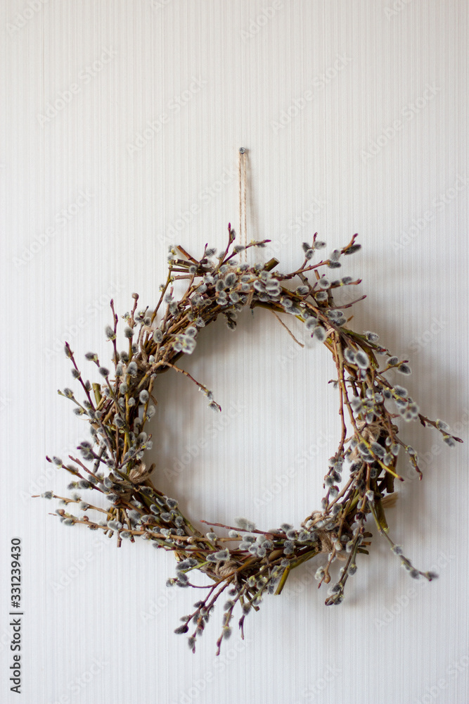 a wreath of willow twigs with fluffy buds made with your own hands hangs on a white wall, vertical frame