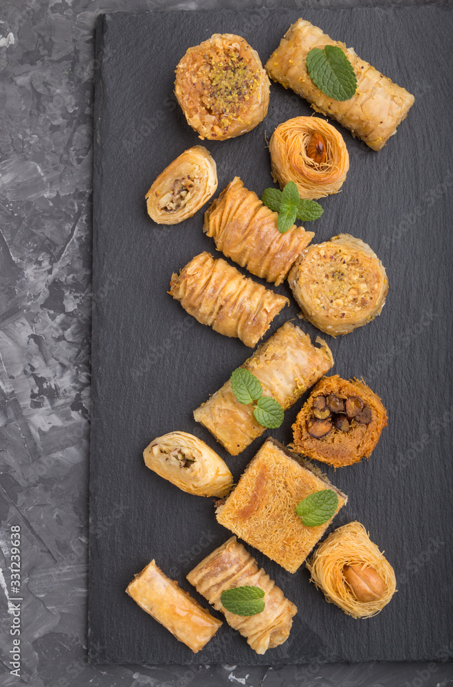 traditional arabic sweets (kunafa, baklava) on a black slate board on a black concrete background.top view, close up.