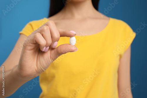 Woman with vitamin pill on blue background, closeup
