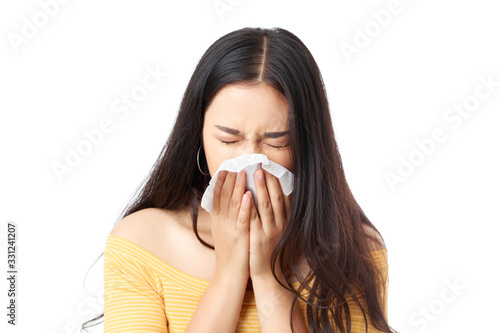 Young pretty Asian woman sneezing, she is using facial tissue paper covering her nose and mouth, head shot studio isolated on white.