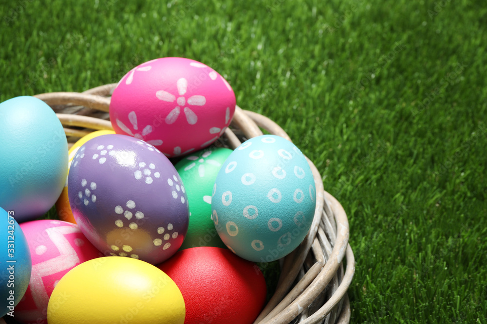 Colorful Easter eggs in decorative nest on green grass, closeup