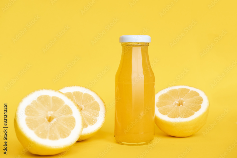 Bottle of lemon juice and fresh lemons. Isolated on yellow background. Copy space Bottle of lemon juice and fresh lemons. Isolated on yellow background. Copy space