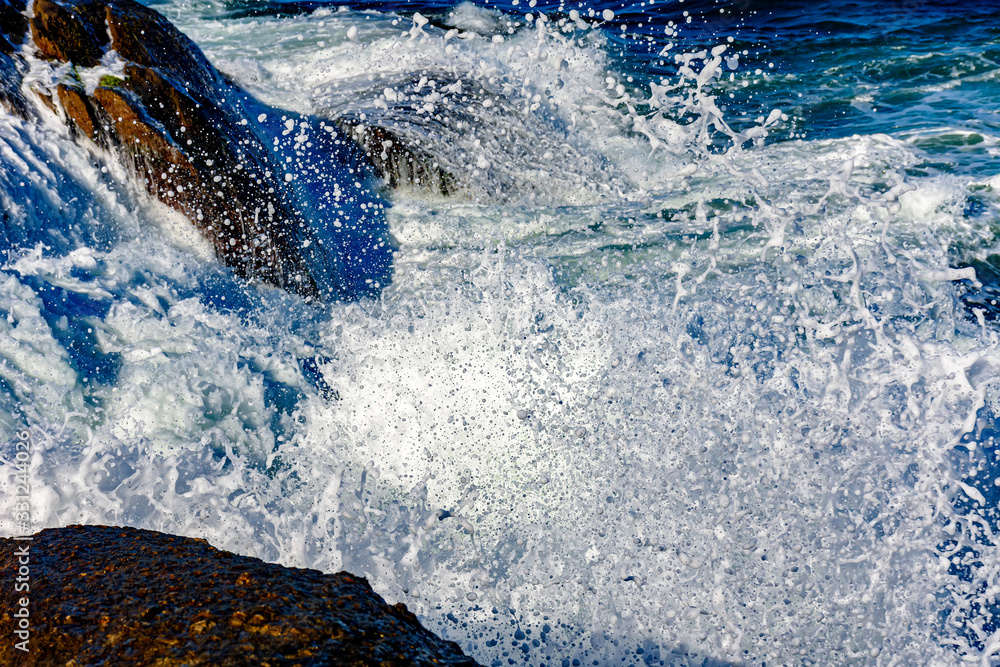 Fototapeta premium Detail of wave breaking over stones with foam, water drops and splash