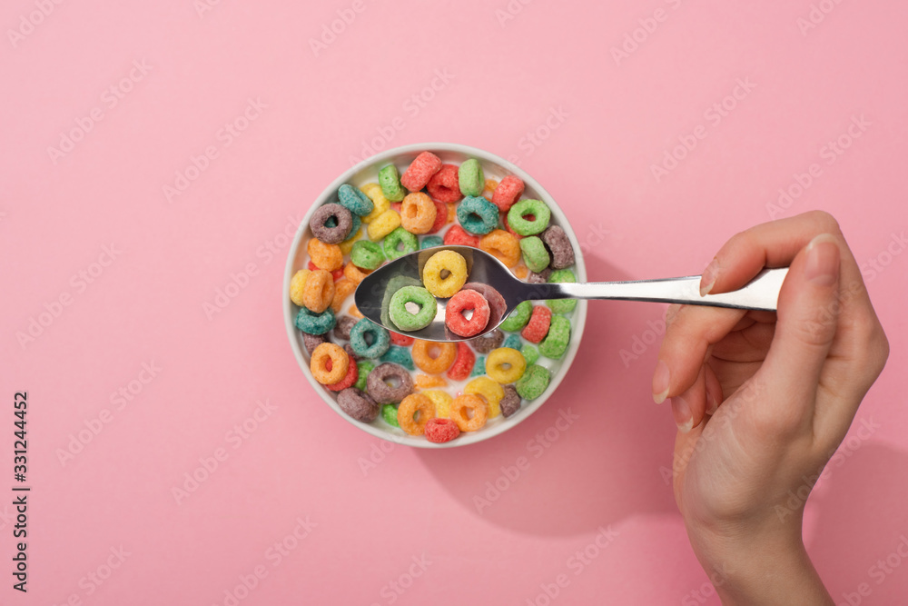 partial view of woman eating bright colorful breakfast cereal from bowl with spoon on pink background partial view of woman eating bright colorful breakfast cereal from bowl with spoon on pink background