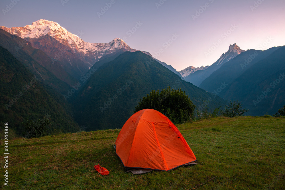 An orange tent with beautiful view of Annapurna mountains range in Annapurna Sanctuary, Nepal at dawn. Annapurna Base Camp Trek is one of the famous trekking routes in Nepal.