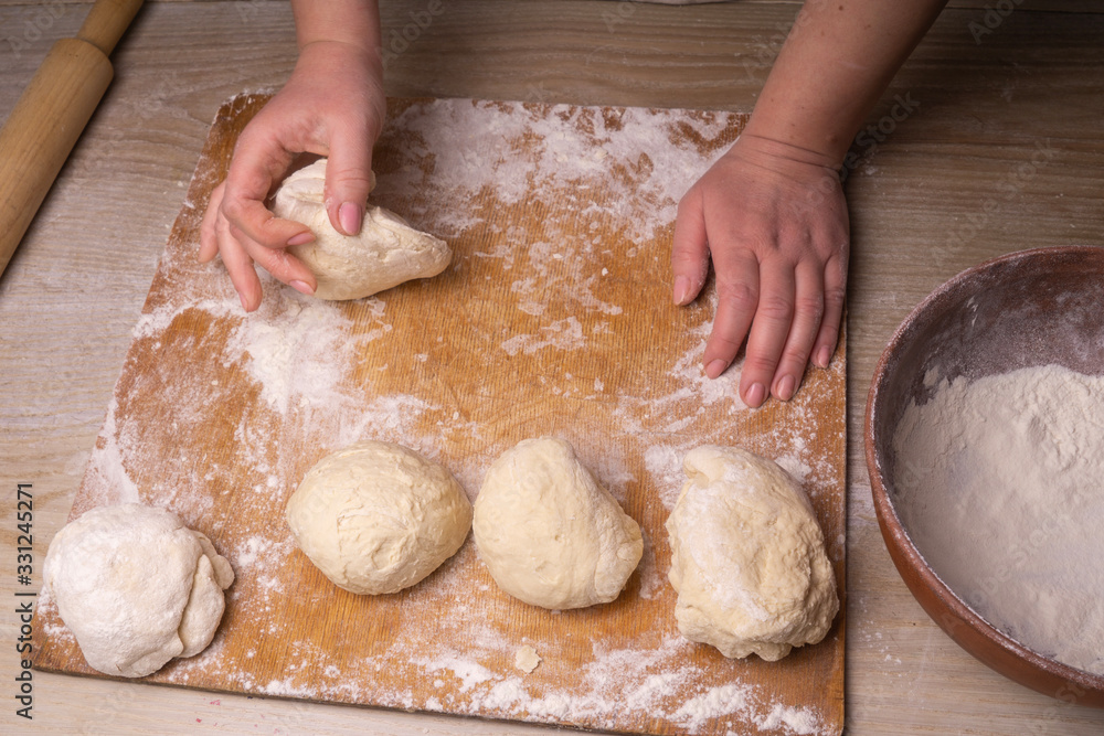 A woman kneads the dough. Plywood cutting board, wooden flour sieve and wooden rolling pin - tools for making dough. A woman kneads the dough. Plywood cutting board, wooden flour sieve and wooden rolling pin - tools for making dough.