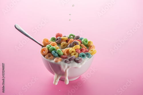 bright multicolored breakfast cereal in bowl with splashing milk and spoon on pink background photo