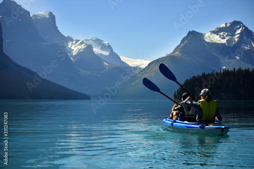 Two people in a double kayak on an aqua green lake in the Canadian rocky mountains