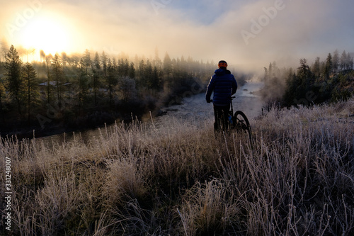 Male mountain biker looking over a foggy river at sunrise