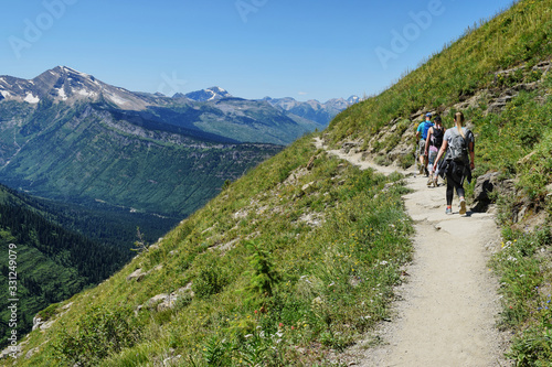 three hikers walking along a trail on a steep grassy mountainside in the alpine