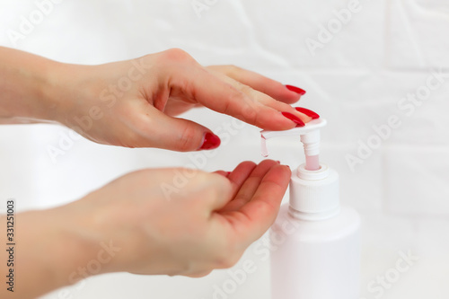 Woman push on dispenser and squeeze out soft soap gel on palm, closeup shot against flat background. Transparent liquid soap used for hand washing photo