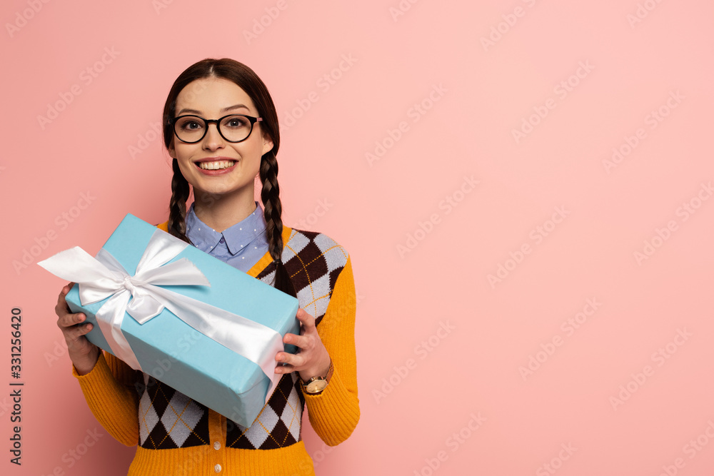 smiling female nerd in glasses holding gift box on pink smiling female nerd in glasses holding gift box on pink