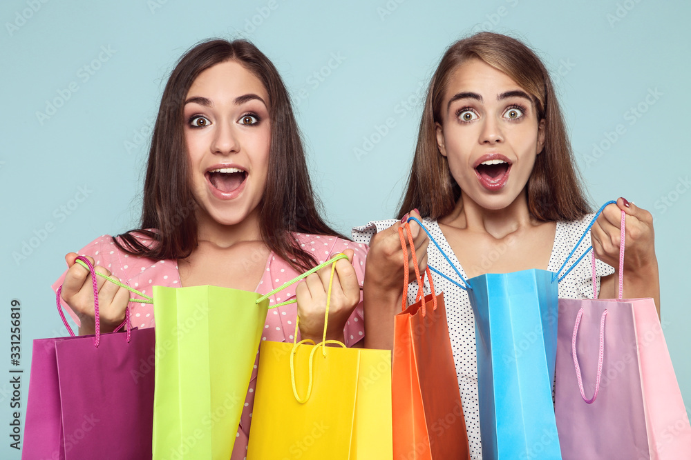 Young happy girlfriends with shopping bags on blue background