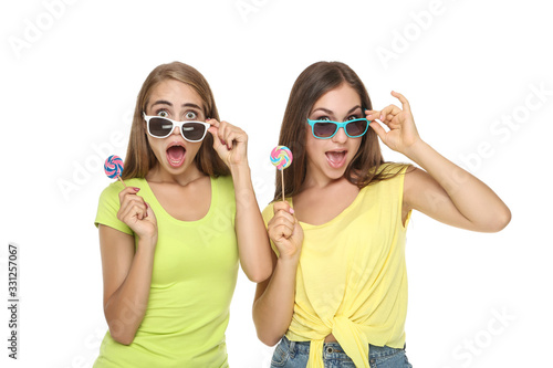 Young happy girlfriends in sunglasses and holding sweet lollipops on white background