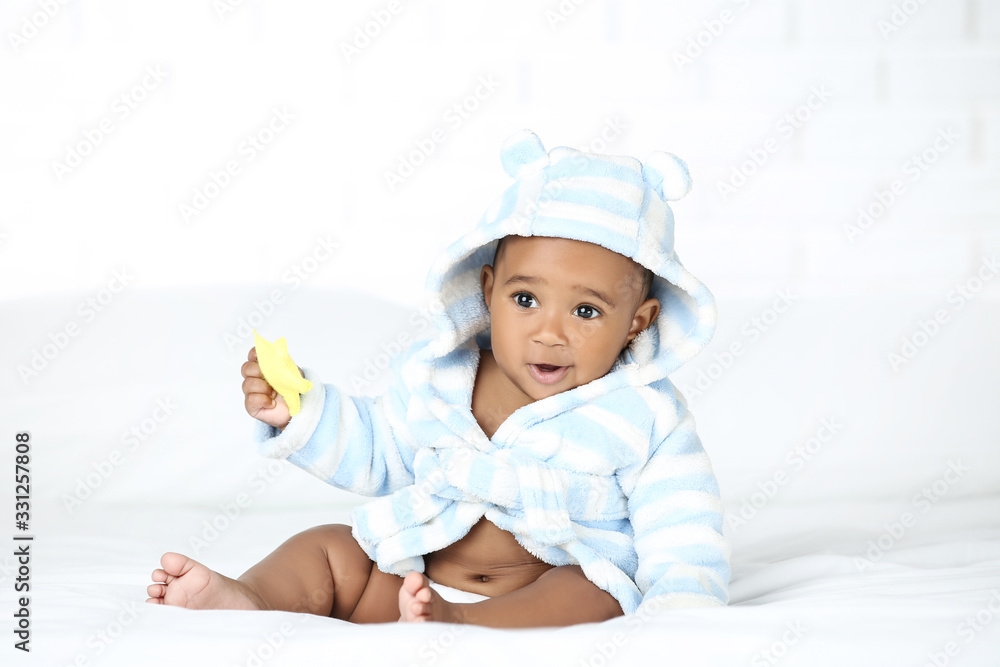 American baby girl in bathrobe sitting on bed and holding toy American baby girl in bathrobe sitting on bed and holding toy