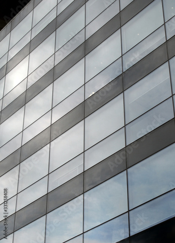 vertical perspective view of the facade of a modern glass commercial building with steel frames and sky reflected in the windows
